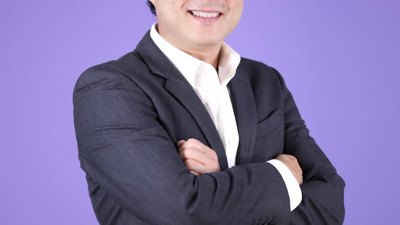 スーツを着たビジネスマンが腕を組み、自信に満ちた笑みを浮かべています。スタジオ照明、固定カメラ、紫色の背景。