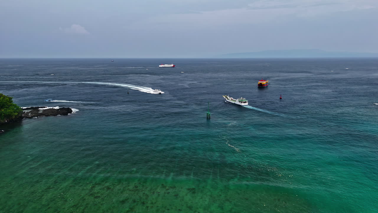 An aerial view flying forward over the vibrant blue waters of Padang Bai Beach, showcasing various boats and coastal features