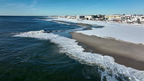 Waves-crash-on-sandy-beach-covered-in-winter-snow