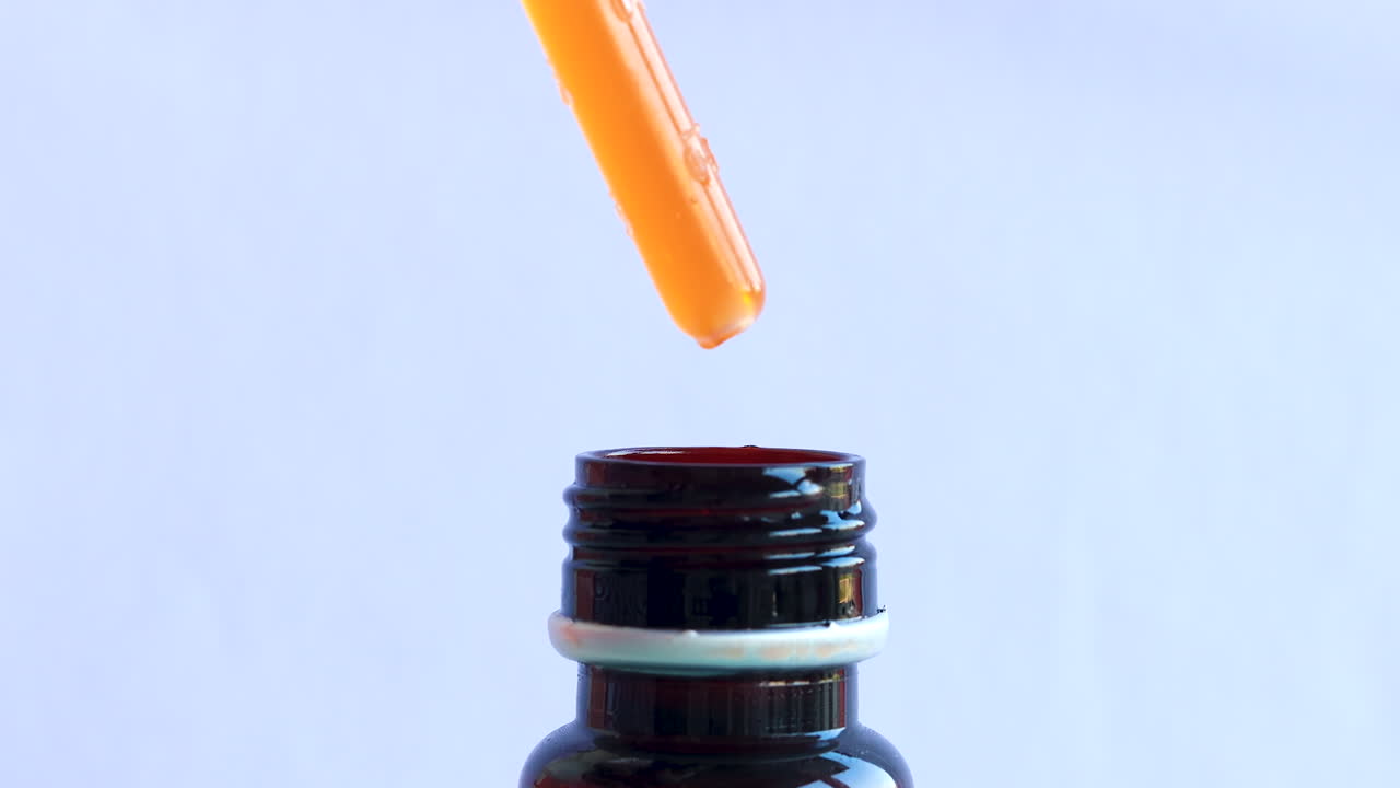 갈색 병에 오렌지 액체 방울을 밀어 피펫의 고립 된 닫습니다