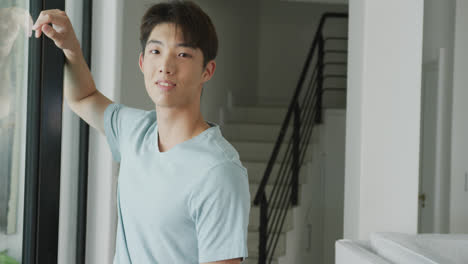 portrait of happy asian male teenager looking away and leaning on window