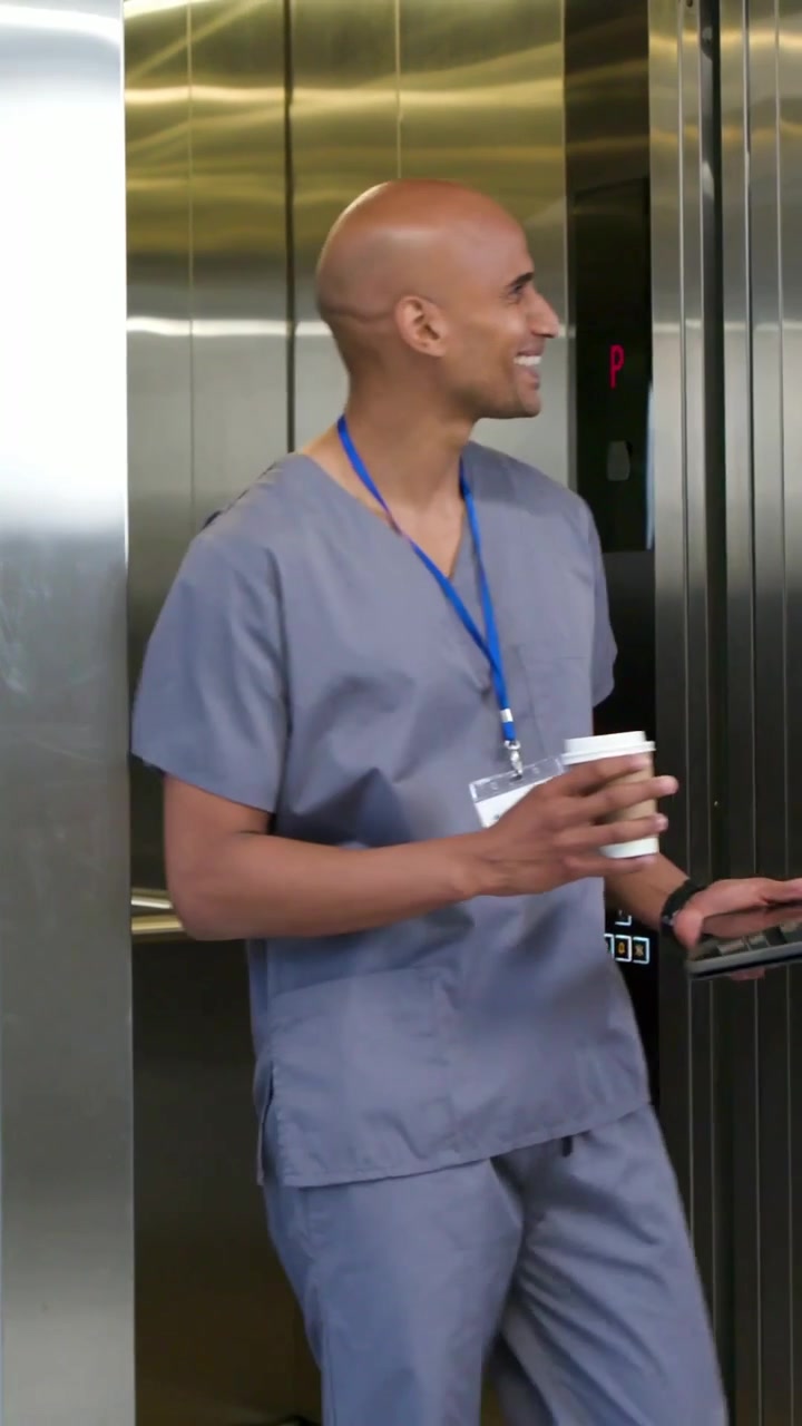Vídeo Vertical: Elevador Abrindo, Equipe de Jaleco Saindo com Café e Tablet Cumprimentando Colega na Clínica