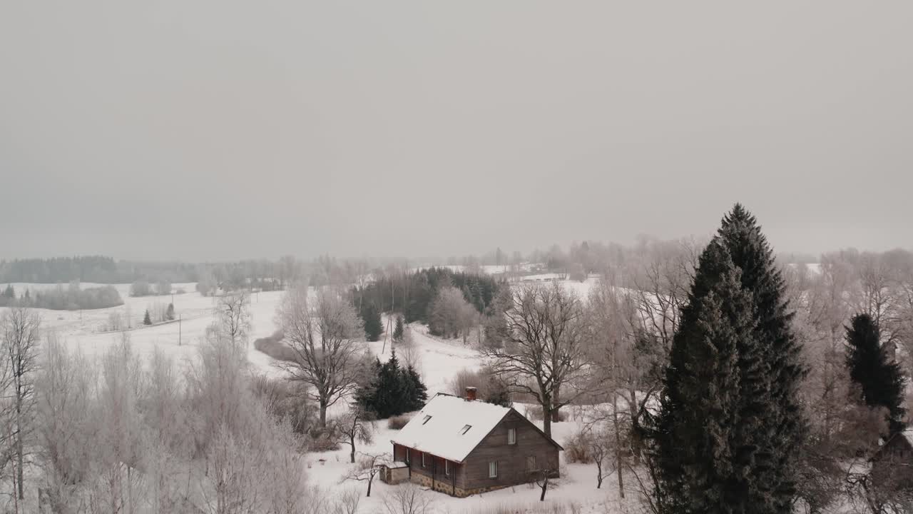 Ascending drone shot of a family home in the countryside on a white winter day with lots of snow and frost on the trees. Aerial drone shot in the suburbs.