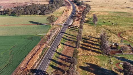 drone footage glides above a quiet gravel road bordered by fields and trees in rural tamworth, new south wales, under bright natural daylight
