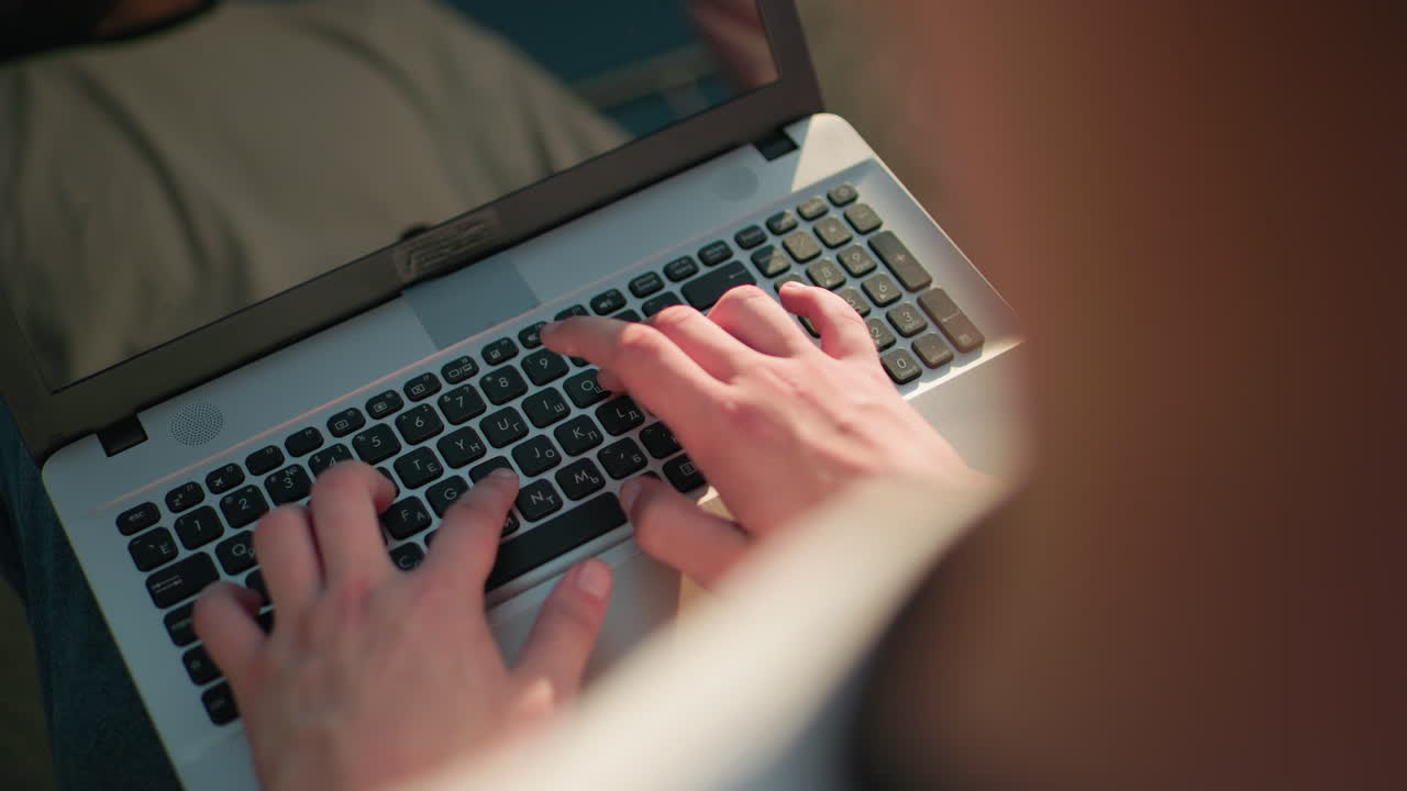 hombre escribiendo en el teclado de la computadora portátil al aire libre, el reflejo de las manos y la luz del sol visibles en la pantalla, creando una escena atractiva y serena, el fondo presenta iluminación sutil y un entorno borroso