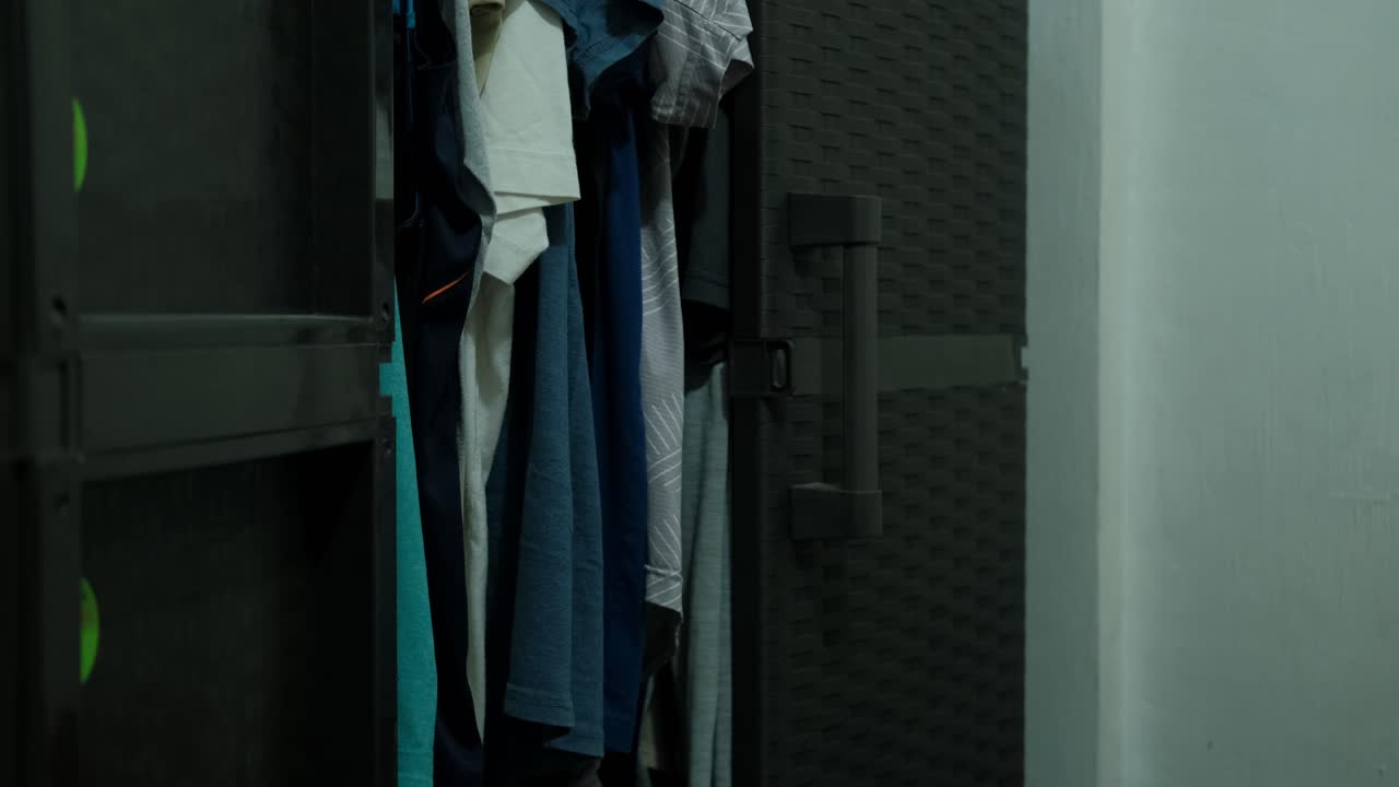 Medium shot of male person opening plastic wardrobe and hanging shirt inside.