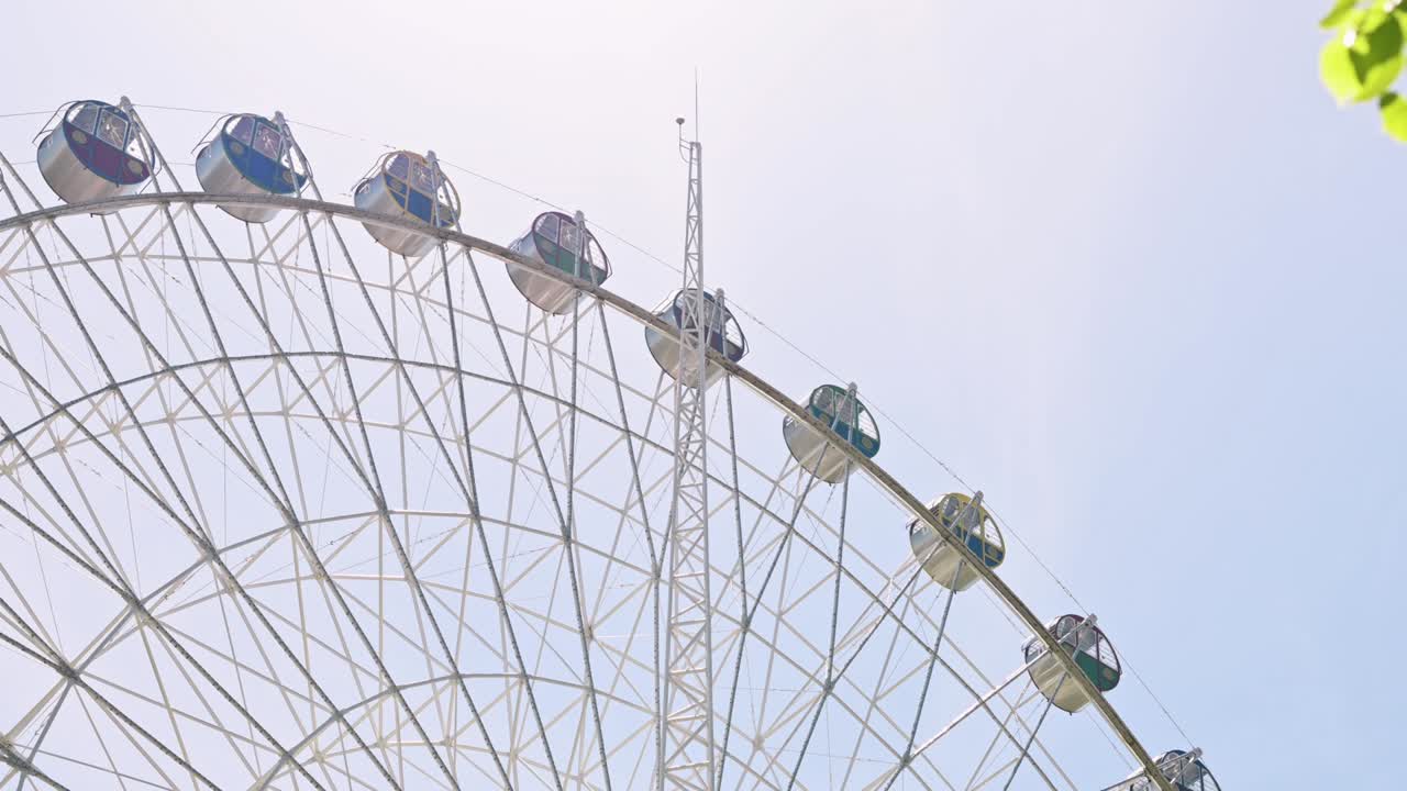 다채로운 오두막을 가진 페리스 의 전망, 공원의 봄 녹색 나무 잎을 통해, 파란 하늘에 대한 도시 페리스 바, 엔터테인먼트 카루셀, 축제, 레크리에이션, 재미있는 활동