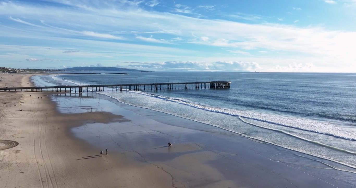Una ripresa aerea cinematografica grandangolare con drone del molo di Santa Monica, che ruota lentamente in avanti sopra la spiaggia e l'Oceano Pacifico, con la costa di Los Angeles in lontananza, in California.