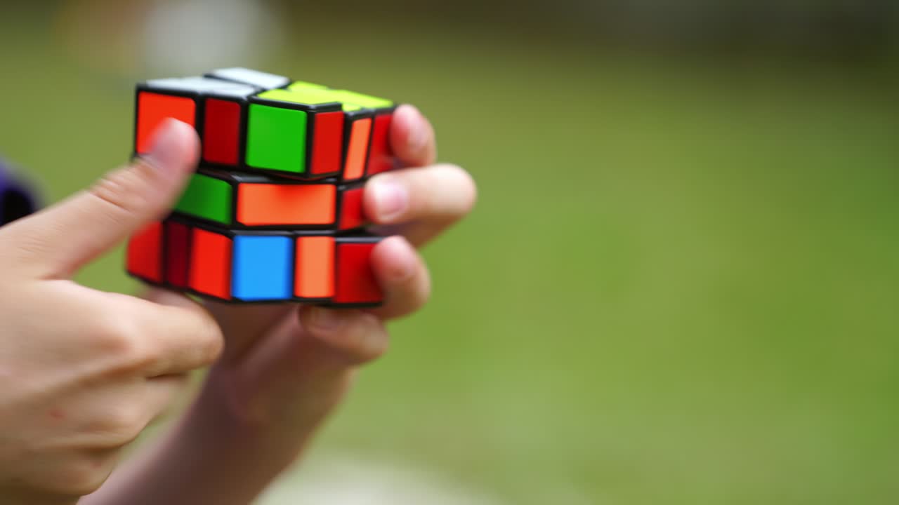 Young person solving a Rubik's cube puzzle. Smart boy tries to finish solving colorful combination in Rubik's Cube on green background. Close-up.