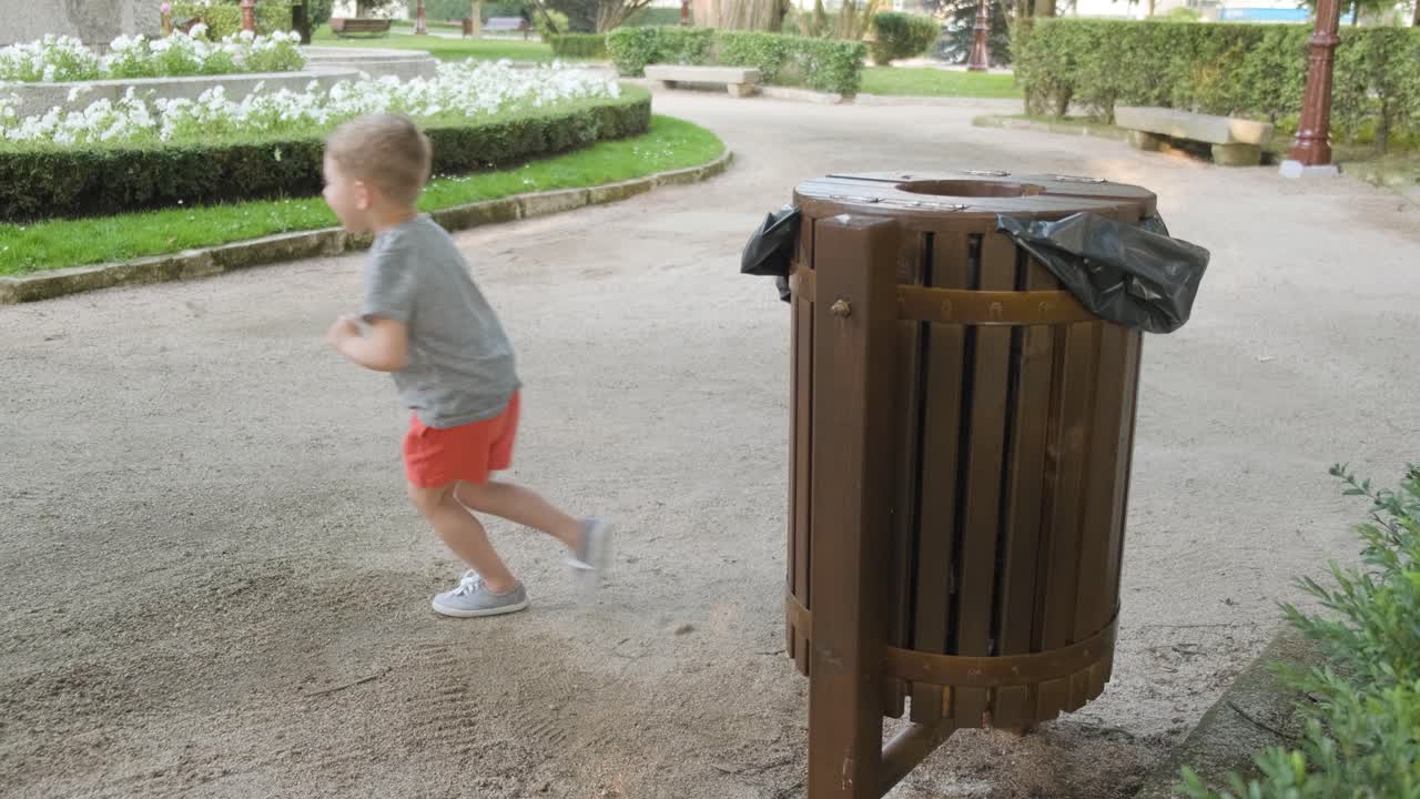 A Young Boy Happily Runs and Throws Rubbish into a Trash Bin, Slow Motion