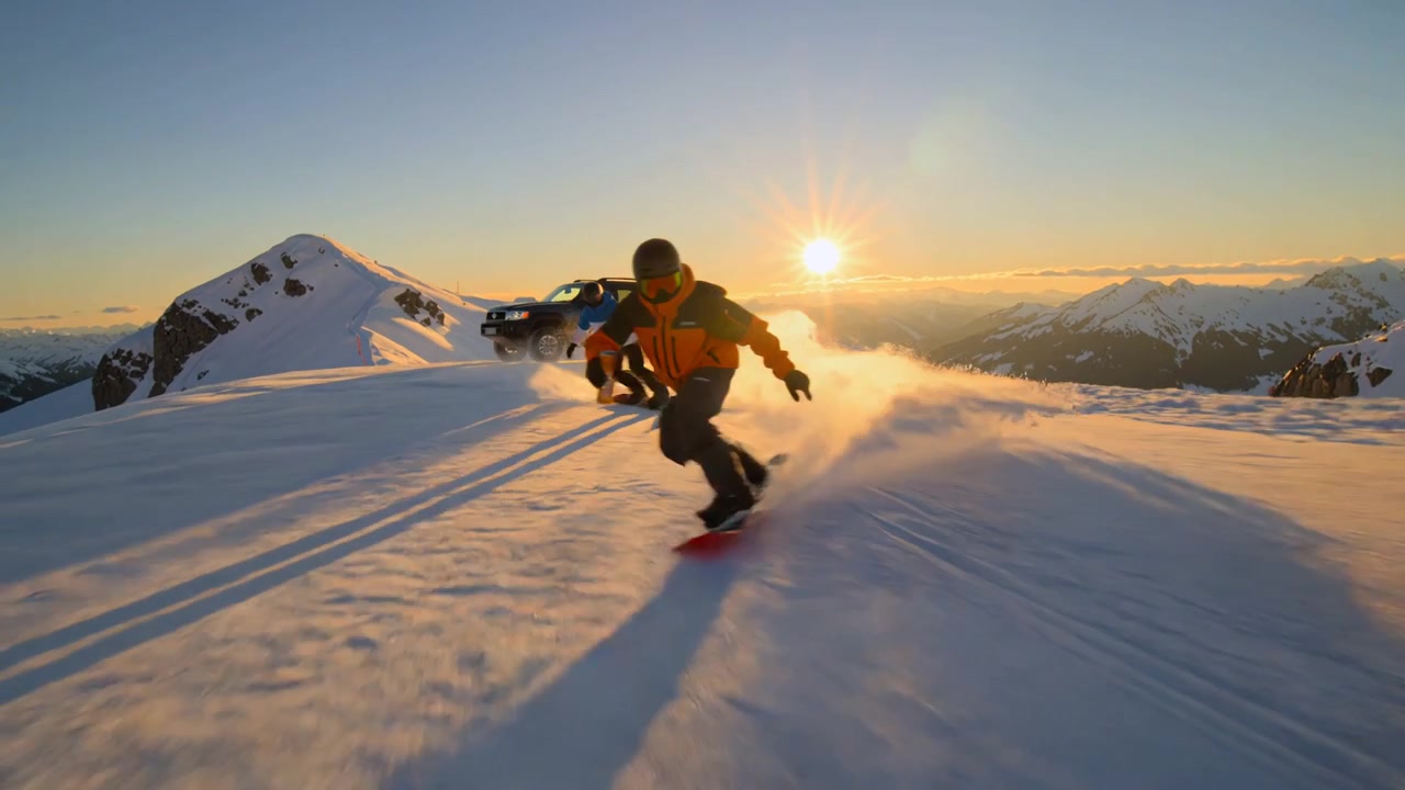 Due snowboarder che fanno carving su una montagna innevata con un SUV al tramonto