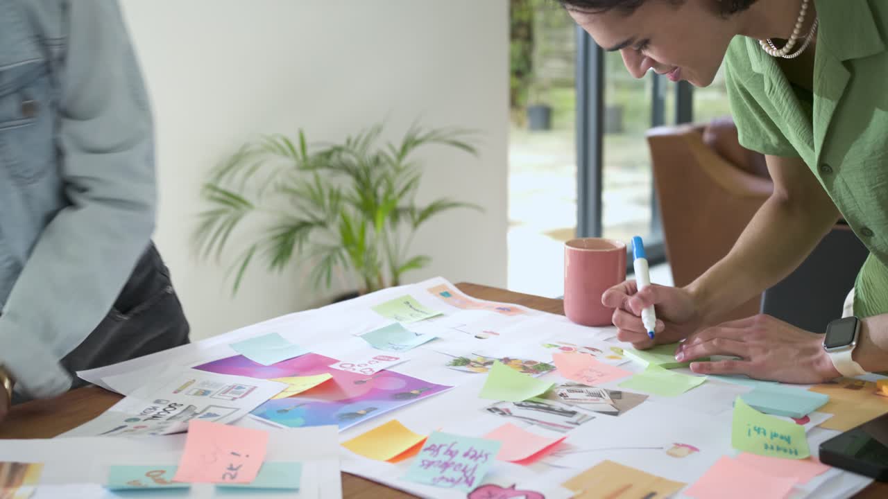 Picking up pink sticky note, African American woman and Asian man brainstorming at home workspace