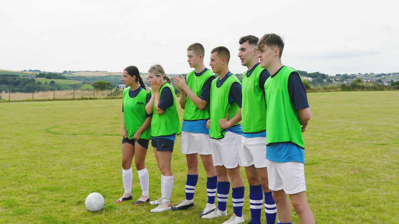 Male and female soccer players staying in row and observing another player on pitch