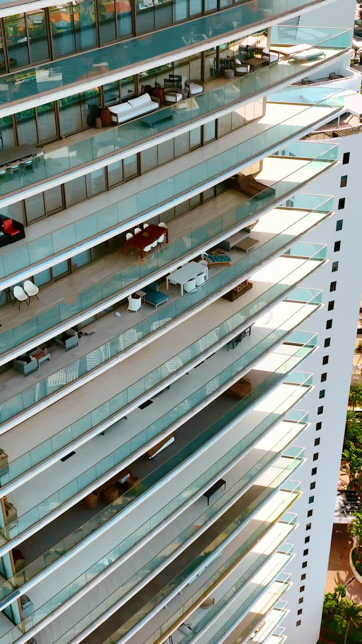 Close view at the facade of a modern high-rise block of flats. Drone going up along the glassy balconies. Miami Beach, Florida, USA. Vertical video