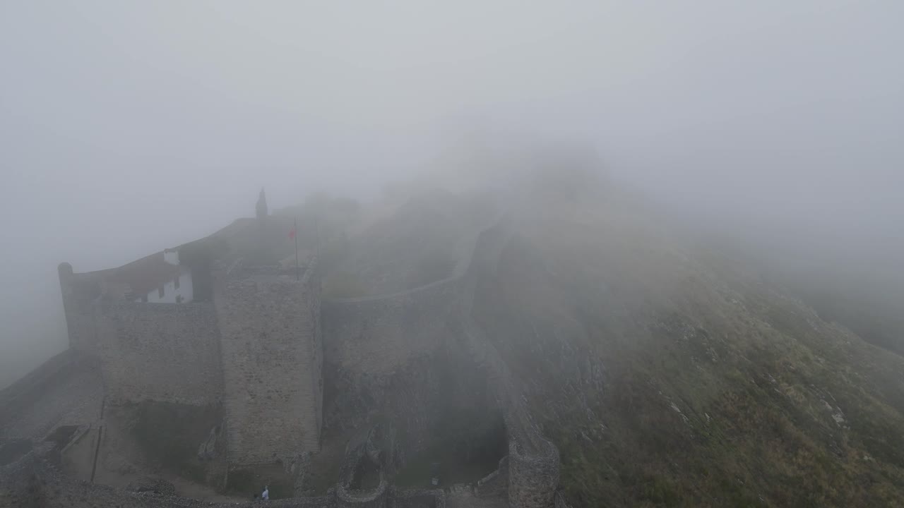 una espesa niebla sobre un castillo medieval es vista por un dron que vuela