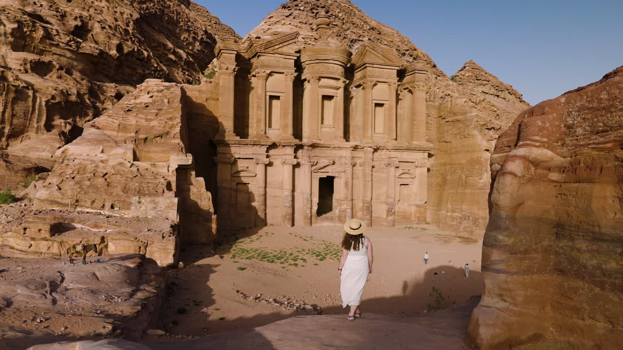 mujer caminando hacia el monasterio de ad deir al atardecer en petra, jordania - disparo de avión no tripulado