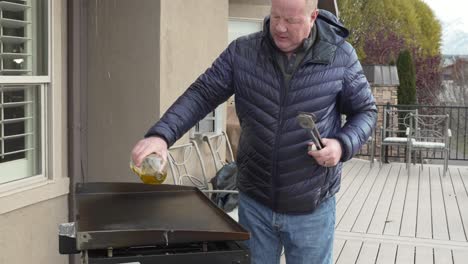 older man pours oil on a hot flat top griddle to season after cooking