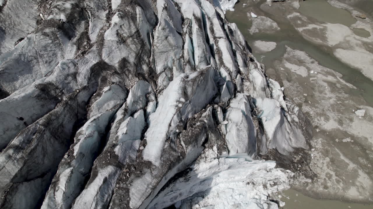 Drone shot revealing Pasterze Glacier and streams of water pouring down the valley walls into the glacier lake in the background