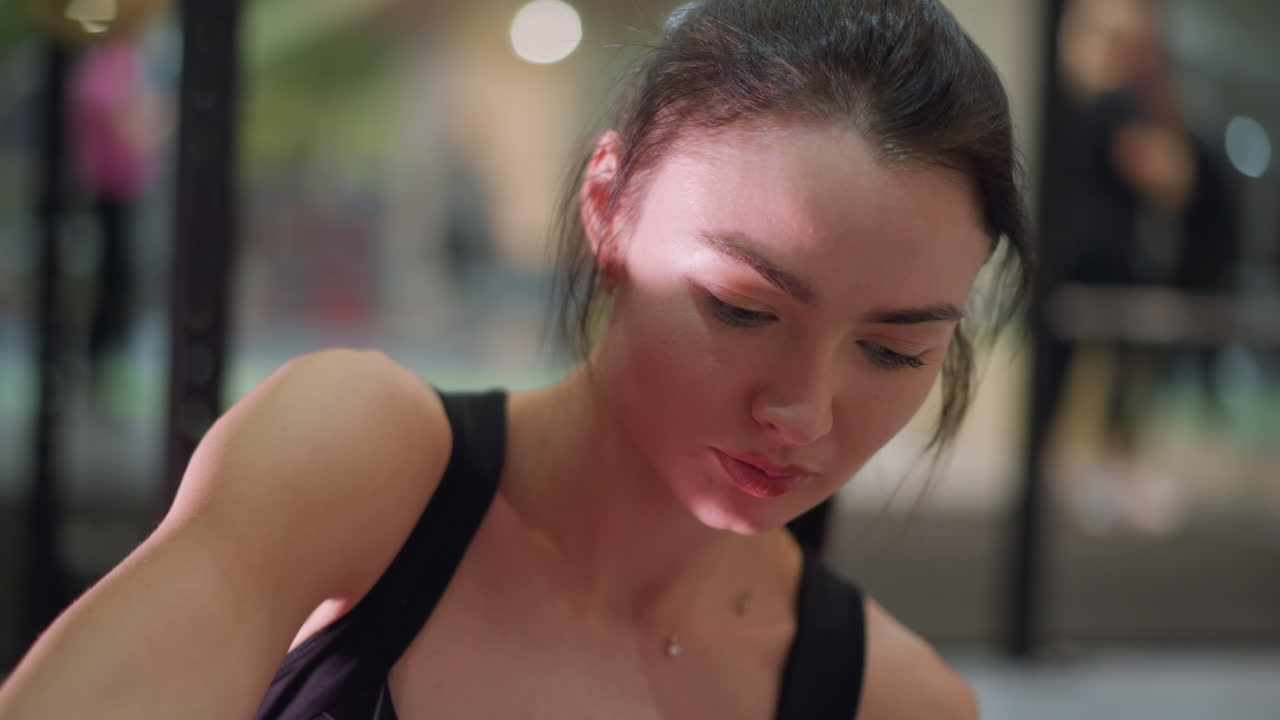 asian woman boxing trainee checking form, closeup of concentrated face between sets, sweatdamp hair, mirror and rings reflecting gym lights, steady breath and subtle fatigue, trainer silhouette