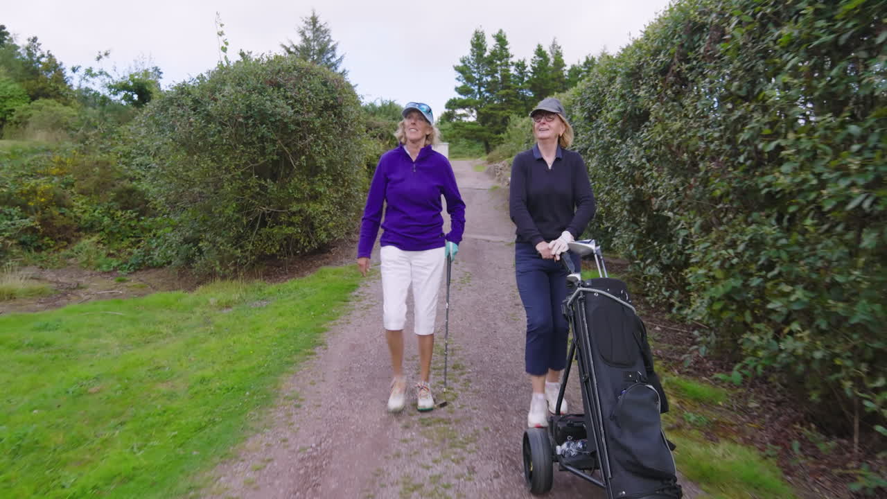 Female golf players walking with clubs and talking on golf course on cloudy day