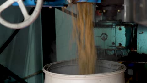 grains falling out of a milling machine. whole farming grains being crushed for processing. brewing beer grains. brewery grains being milled.