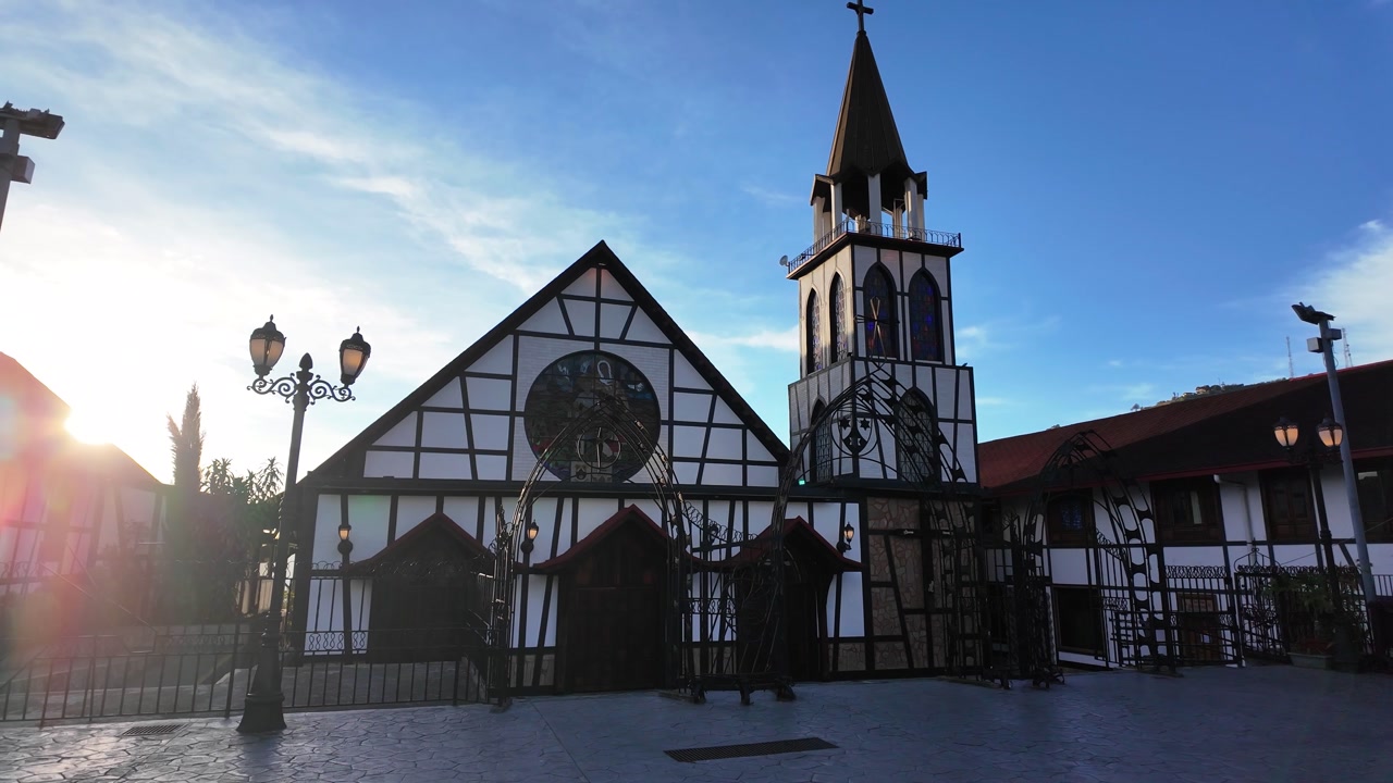Sunrise with soft golden light illuminating half-timbered architecture, historic structure features a tall tall bell tower, rustic wooden details, and peaceful plaza setting, town’s European heritage