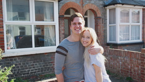 portrait of young couple standing outside new home in urban street