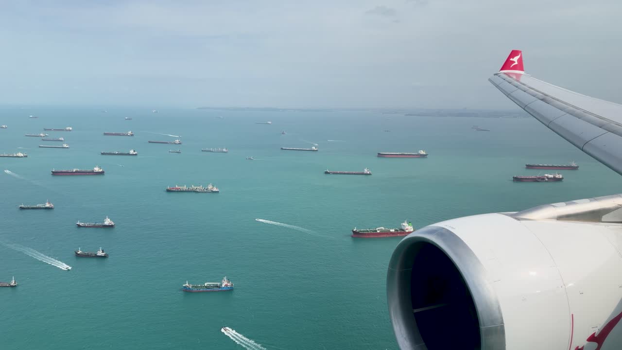 Prospettiva aerea da un finestrino di un aereo che mostra numerose navi da carico ancorate nello Stretto di Singapore.