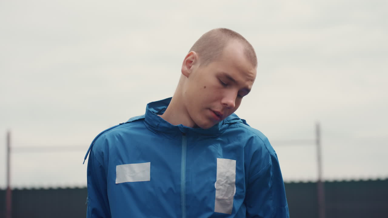 closeup player with steady determined gaze, tight framing on face and blue jacket, urban highrise backdrop and fenced court, subtle sweat and jaw tension, breathing control and pregame composure
