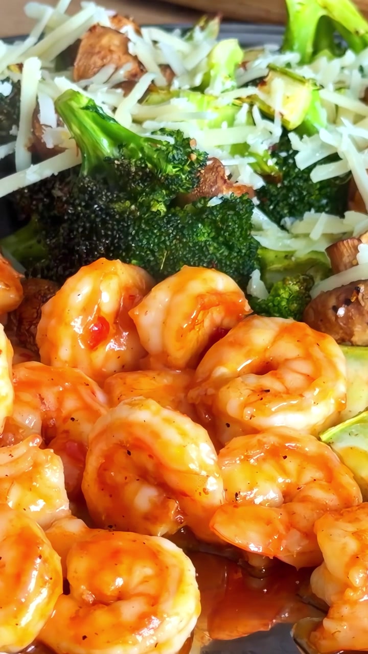 Video verticale ravvicinato di gamberi cotti con salsa, broccoli arrostiti e formaggio serviti su un tavolo da cucina.