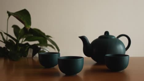 minimal background of a green japanese tea set with steam coming out of the cups, on a wooden table, with a plant in the back