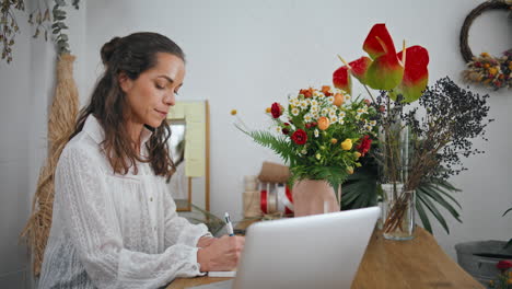 empresario enfocado trabajo flores mesa de la tienda. mujer florista escribir notas en la tienda