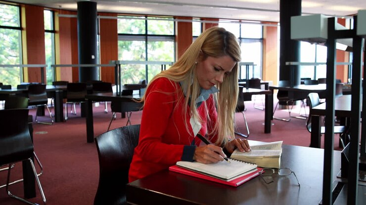 Voksen studerende med læsebriller studerer ved et biblioteksbord