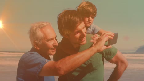 Animación-De-Bokeh-Sobre-Feliz-Abuelo,-Padre-E-Hijo-Tomándose-Selfie-En-La-Playa