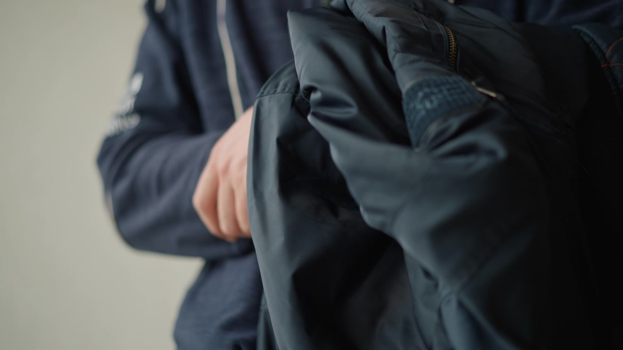Nærbilde av en mann som holder og undersøker mørkeblått stoffmateriale, sannsynligvis klær eller tekstil. Mannens hender er synlige mens de manipulerer den myke teksturen med subtile bevegelser som viser detaljer.