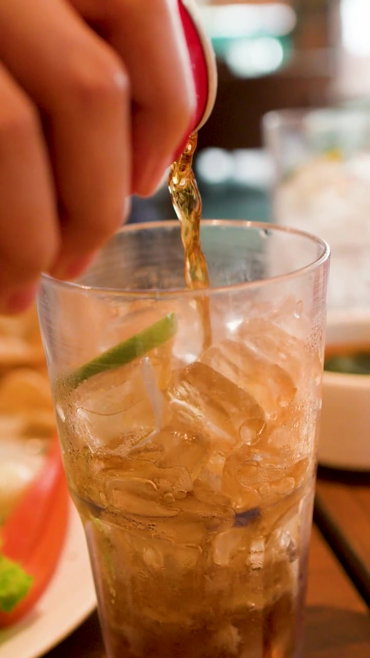 Versare cola in un bicchiere con ghiaccio e lime.