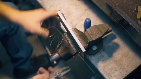 jeweler pulls gold wire through tool in bench clamp closeup