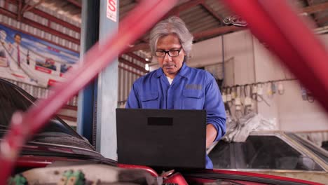 el mecánico repara el daño usando el pc debajo del capó en el servicio de automóviles, concepto de servicio de vehículos.