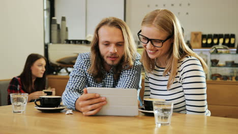 Kaukasische-Glückliche-Freunde,-Die-Sich-Unterhalten-Und-Ein-Video-Auf-Einem-Tablet-Ansehen,-Das-An-Einem-Tisch-In-Einem-Café-Sitzt