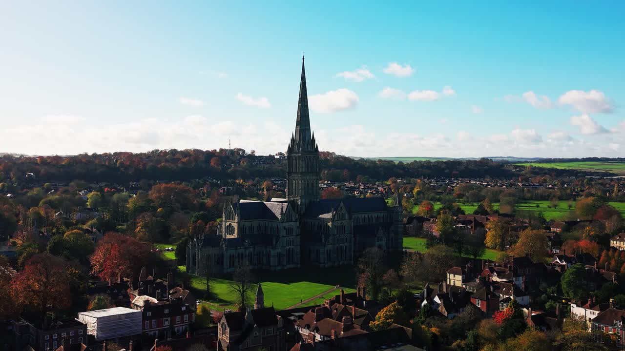Luftdroneoptagelse af Salisbury Cathedral med dens ikoniske spir, der rejser sig over byen omgivet af historiske bygninger og landskab i England