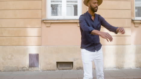 happy afro caribbean man with panama hat dancing latin choreographies alone in street