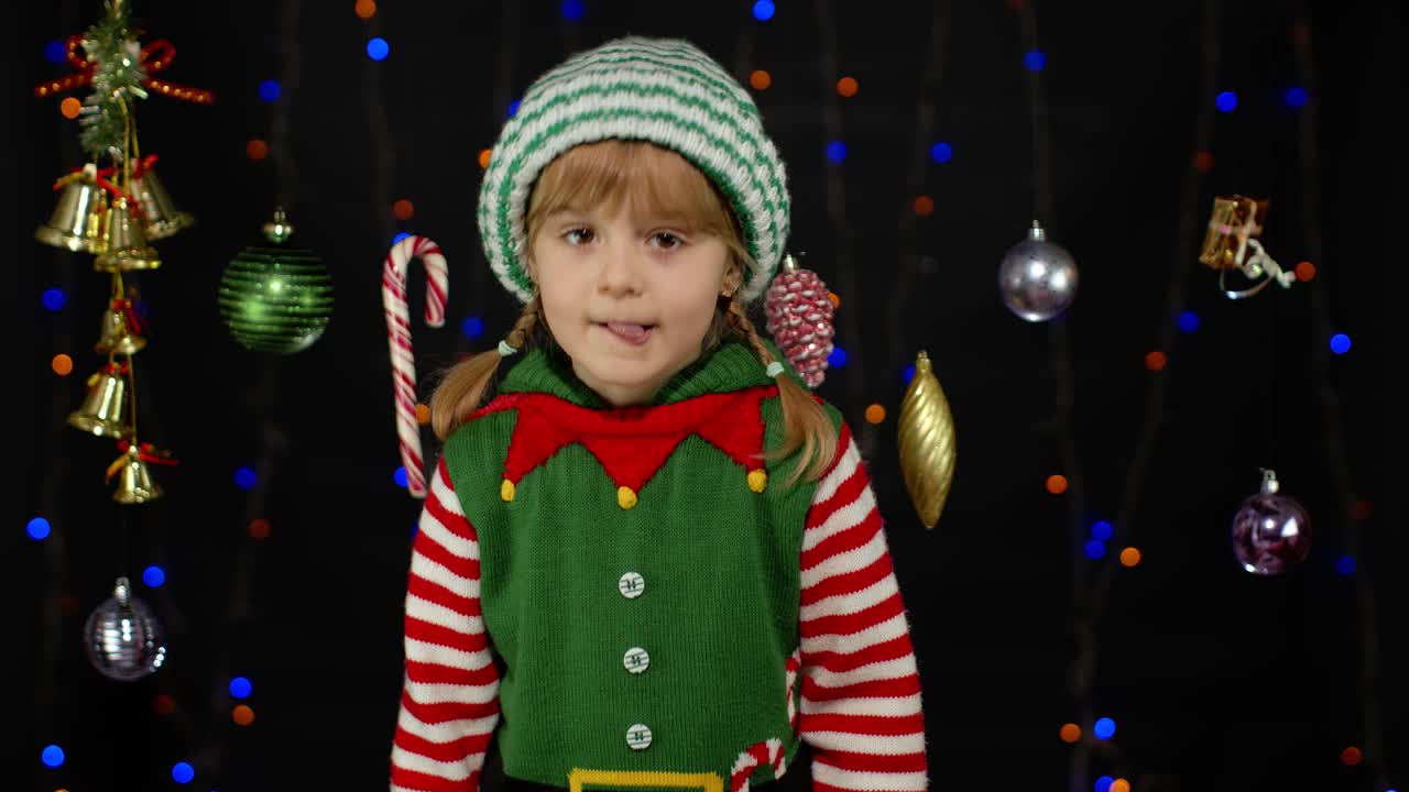 Kid girl in Christmas elf Santa helper costume receiving lollipop gift candy cane. New Year holiday
