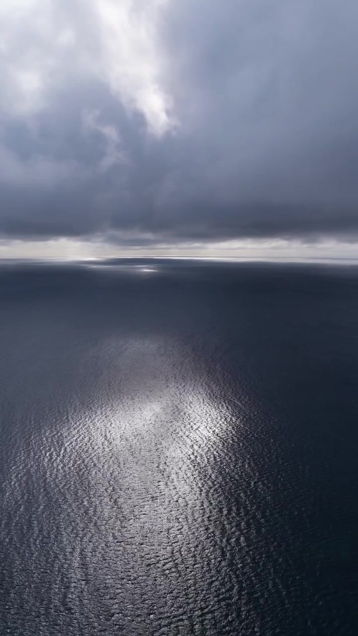 Aerial View Of A Deep Blue Ocean With Shimmering Sunlight Reflecting Off The Water's Surface. - vertical shot