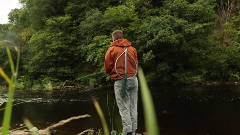 toma de ángulo bajo de un pescador de mosca atrapando una trucha en un arroyo de flujo rápido en escocia