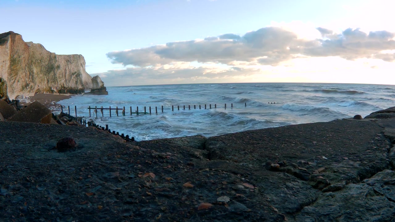 Scogliera di gesso e spiaggia rocciosa che mostrano frangiflutti in legno e onde sotto un drammatico cielo serale lungo la costa di Brighton in Inghilterra durante il tramonto