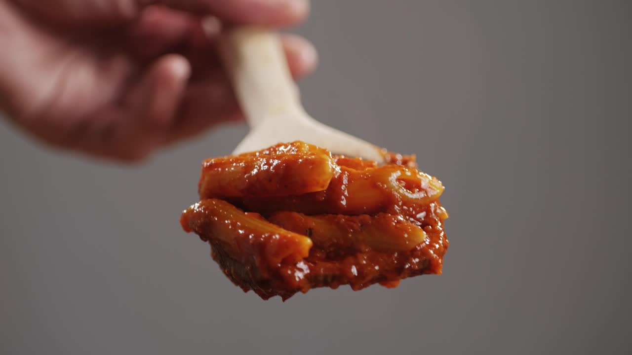 Traditional arrabbiata pasta on wooden spoon, penne with tomato sauce close-up. Cook classic homemade Italian tomato sauce for pasta and pizza in the pan. Chef cooks traditional Italian food. High quality 4k footage