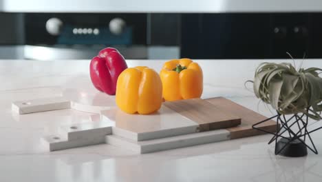 three vibrant bell peppers rest on stacked marble and wood cutting boards under bright kitchen lighting.