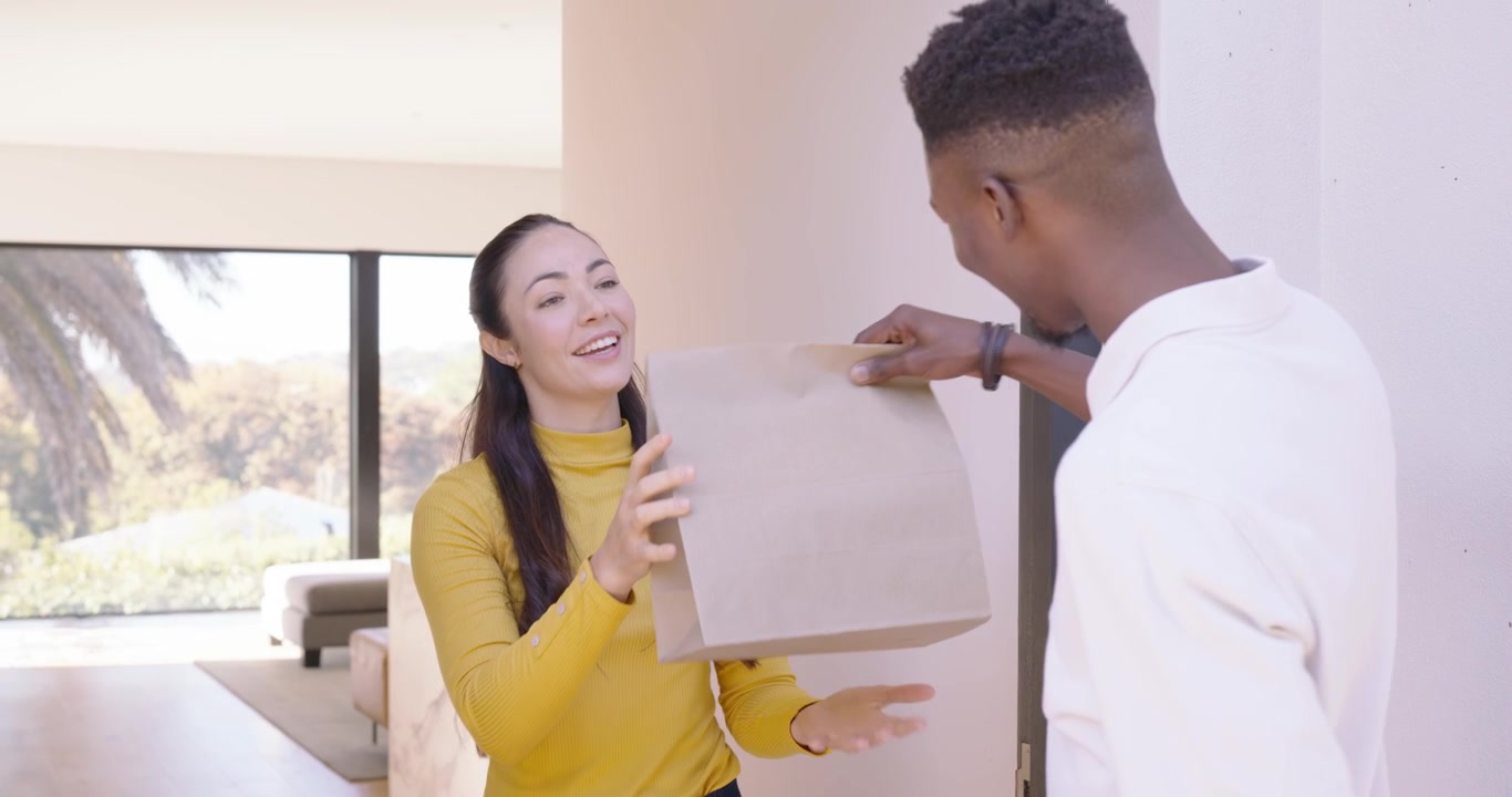 Fattorino multietnico e donna residente con un top giallo che apre la porta, firma sul tablet, con un pacco e spazio per il testo.