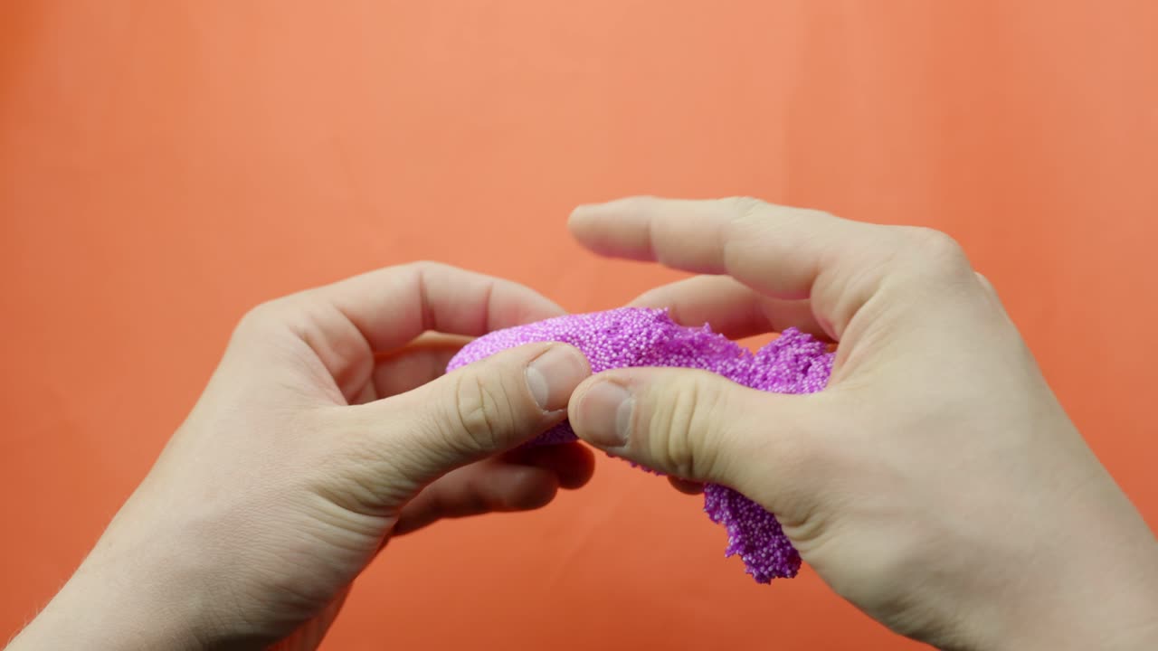 Stretching pink floam slime between hands on orange background, playful and tactile scene
