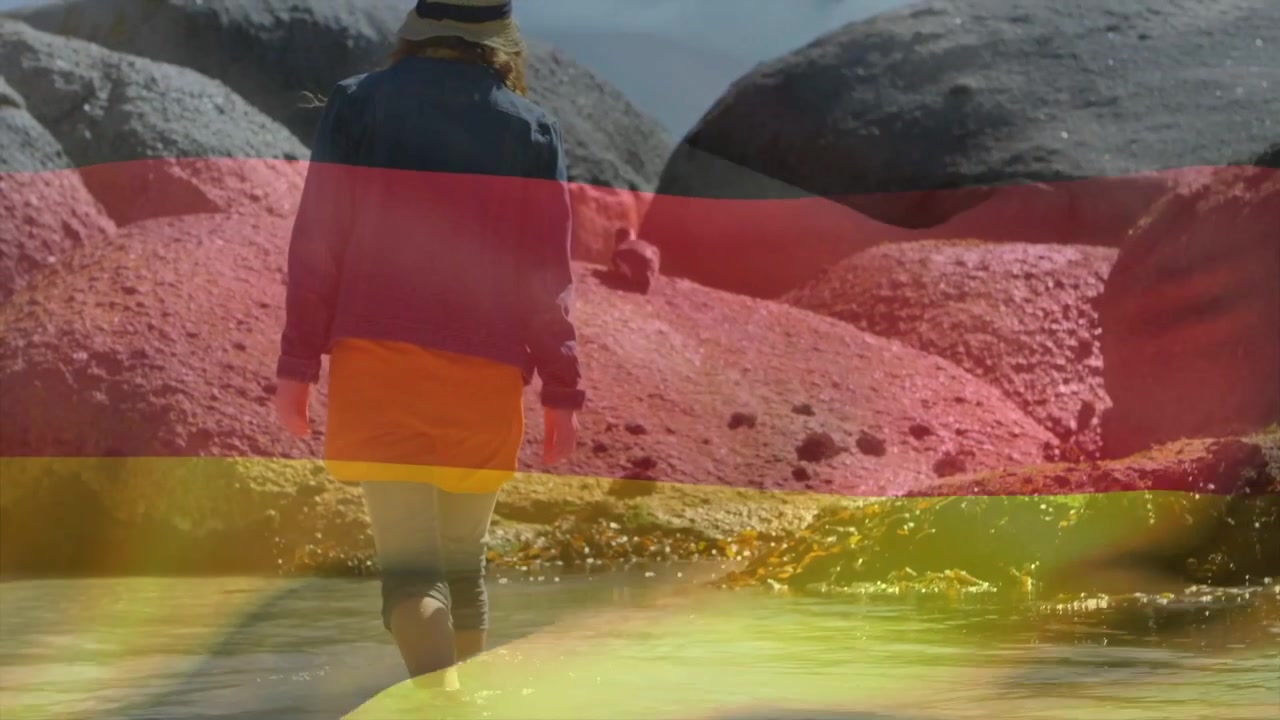 Video verticale: Inizio clip che mostra una donna con cappello da sole e gonna arancione che guada verso rocce con fasce.